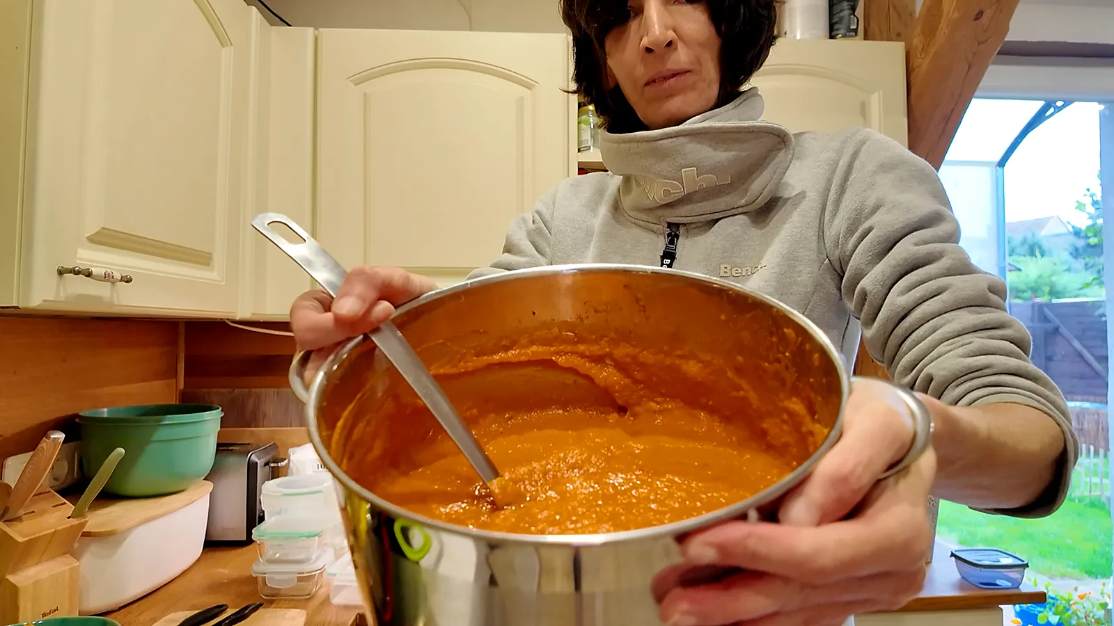 Großer Topf mit cremiger, orangeroter Kürbis-Tomatensoße und Schöpfkelle in der Küche